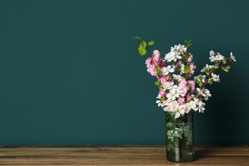 Vase with beautiful blooming branches on wooden table near green wall