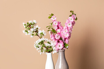 Ceramic vases with beautiful blooming branches near beige wall, closeup