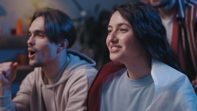 Happy girl with Qatar flag celebrating and screaming near her happy friends while watching football game on TV. Friends sitting on sofa and supporting team with cheery emotions.