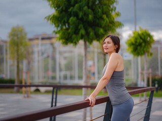 outdoor sports, workout and wellness concept. asian young strong, confident woman in sportive clothes Relaxing After Fitness Workout In Park.