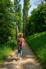Woman with brown hair, gray t-shirt, jeans, straw hat and red backpack hiking in the nature in...