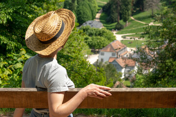 Woman with brown hair, gray t-shirt, jeans and straw hat  sitting on a park bench in the sun, looking at Staatspark Fürstenlager, Auerbach, Bensheim, Germany