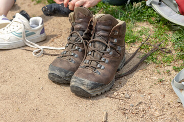 Two brown used hiking shoes standing on a hiking trail next to a meadow, woman changing her shoes