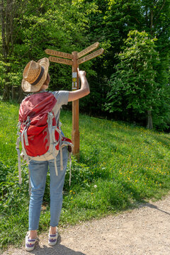 Woman with straw hat and red backpack pointing her finger on a wooden way sign at Staatspark F&uuml;rstenlager, Luisendenkmal, Neun Aussichten, Apfelallee, Eremitage, Auerbach, Bensheim, Germany