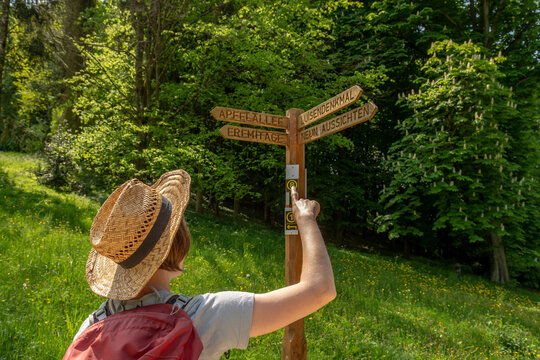 Woman with straw hat and red backpack pointing her finger on a wooden way sign at Staatspark F&uuml;rstenlager, Luisendenkmal, Neun Aussichten, Apfelallee, Eremitage, Auerbach, Bensheim, Germany