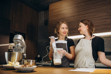 Two nice cute lovely sweet attractive charming cheerful women blonde cooking good vegan vegs food in modern kitchen and they blog about how to eat right