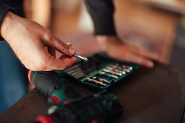 Close up of male hands holding a drill bit, leaning on the desk.