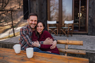 Portrait of a couple in a hug, sitting in front of their home.