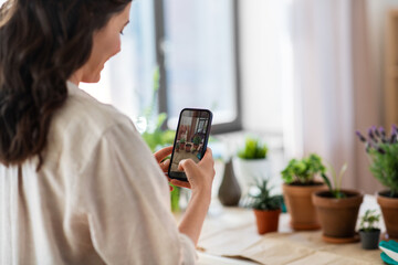 people, gardening and housework concept - happy woman with smartphone photographing pot flowers at home