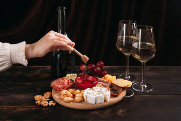 Woman's hand takes a piece of cheese from the Appetizers board with assorted cheese, meat, sausage rosette, grape and cookies