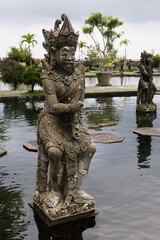 Fototapeta na wymiar Exquisite ancient monument on indonesian culture, history and balinese religion - stony statue of human warrior deity or demon in beautiful Tirta Gangga park on Bali, vertical. Amazing travel on Bali.