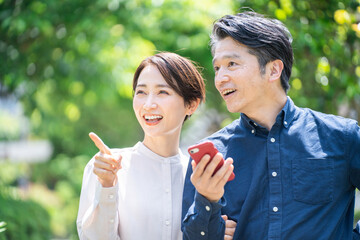 Fototapeta premium スマホで道を探すミドル夫婦（カップル・屋外・新緑・笑顔）