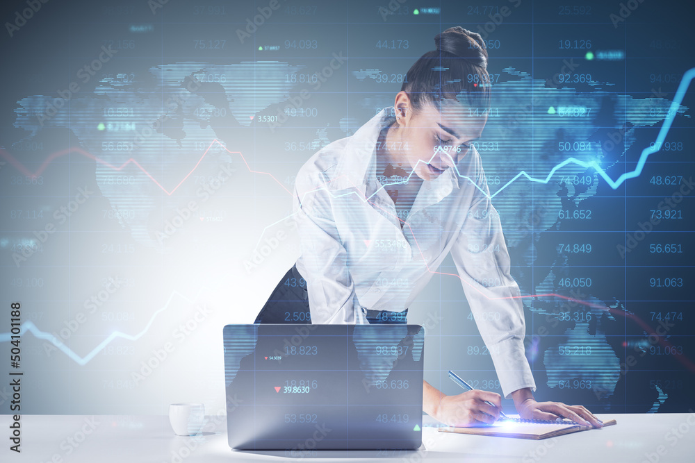 Poster trading and investing concept with young businesswoman making notes in a book in front of laptop and