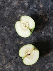 Two halves of green apple on black concrete background with copy space.