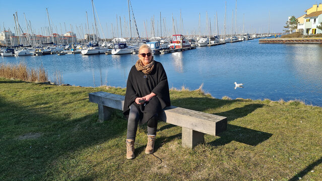 Portrait of a blonde woman wearing sunglasses sitting on a bench in the marina