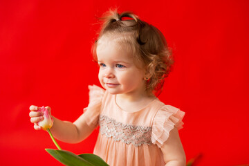 girl is fair-haired curly with a flower tulip. Child in a beautiful pink dress on a red background