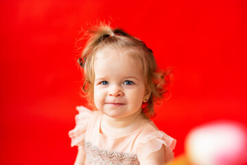 girl is fair-haired curly with a flower tulip. Child in a beautiful pink dress on a red background