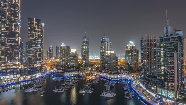 Luxury yacht bay in the city aerial night panoramic timelapse in Dubai marina. Modern tallest skyscrapers along waterfront promenade and boats floating in harbor