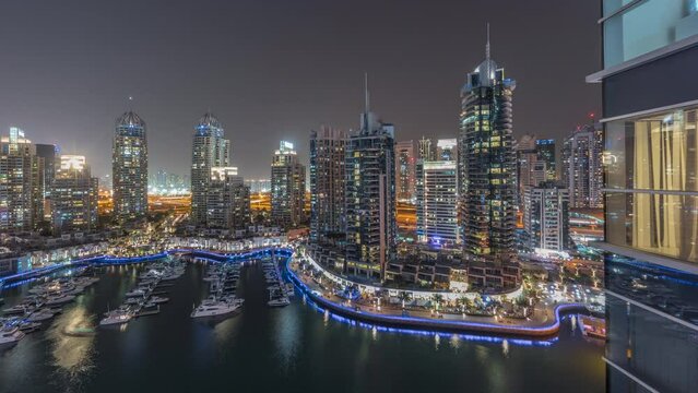 Luxury yacht bay in the city aerial night timelapse in Dubai marina. Modern skyscrapers along waterfront promenade and boats floating in harbor panoramic view