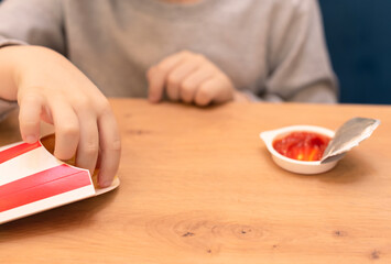 Child boy eating his French fries with ketchup in the cafe. Junk food, unhealthy eating concept