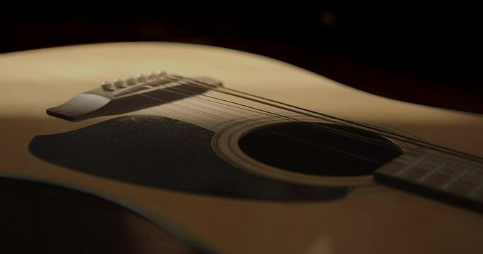 A shadow slowly darkens the body of the acoustic guitar