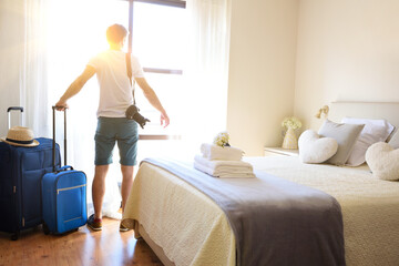 Man with suitcases looking out a window in hotel room
