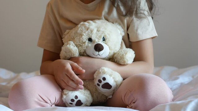 A little girl plays with soft toys sitting on the bed.