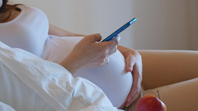 A pregnant woman is holding her phone and chatting on social media.