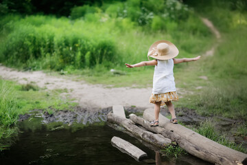 girl child cross the logs of a stream in forest, summer time