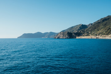Fototapeta na wymiar Beautiful seascape with blue sky, smooth water surface and rocky cliffs in Liguria coastal area. Popular italian travel destination.