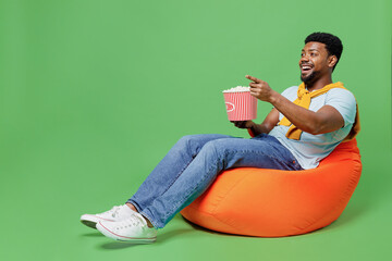 Full body laughing fun young man of African American ethnicity wear blue t-shirt sit in bag chair...