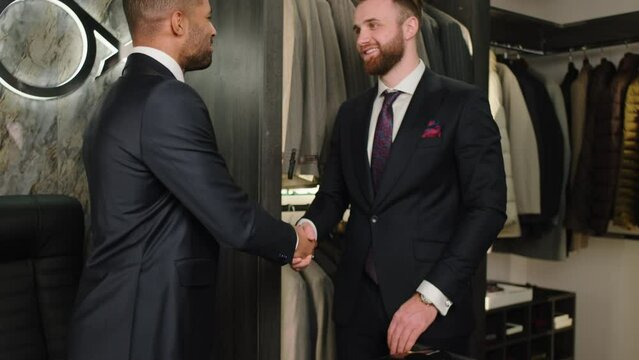 Handsome Afro American businessman make a deal with the designer from the suit shop they shaking hands and smiling large