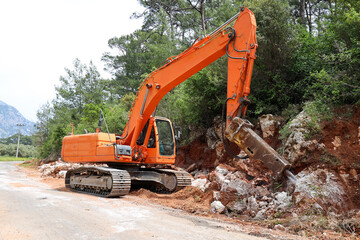 Fototapeta na wymiar Excavator crusher machine breaks rocks to widen road