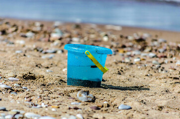Isolated Blue Kid 's Bucket Toy Left on the Sand at the Beach by the Sea. Pebbles All Around. 