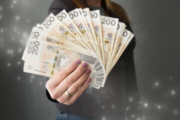 Polskie banknoty 200zł trzymane w dłoni, kobieta daje plik pieniędzy - obrazy, fototapety, plakaty