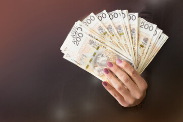 Polskie banknoty 200zł trzymane w dłoni, kobieta daje plik pieniędzy
