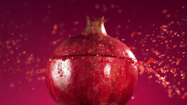 Half Pomegranate falling and splashing on fuchsia background. Food levitation concept. Slow Motion