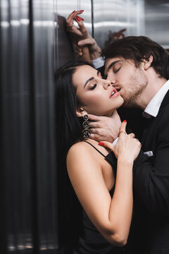 Sexy man kissing and touching neck of seductive girlfriend in elevator.