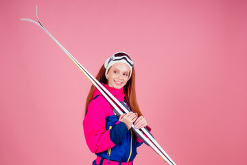 Portrait of sexy smiling redhaired ginger woman in warm clothes professional skier in studio pink background.knitted headband ,warm overalls