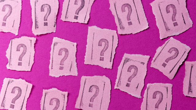 Question marks rubber stamp font letters on torn paper pink background.