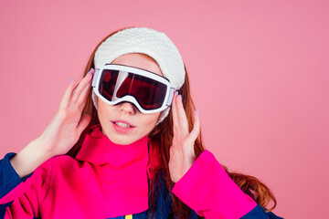 Portrait of sexy smiling redhaired ginger woman in warm clothes professional skier in studio pink background.knitted headband ,warm overalls