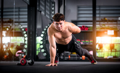 Naklejka na ściany i meble Determined athletic guy in sportswear exercise doing push ups by one hand as part of CrossFit bodybuilding training at gym is Muscular body building in fitness lifestyle.