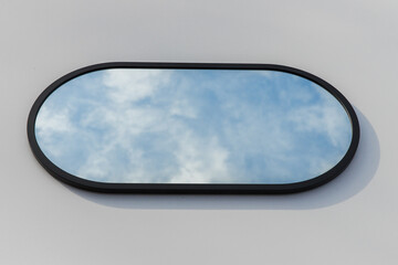 A round or oval mirror with a reflection of the blue sky and white clouds. Close-up. Isolated on a...