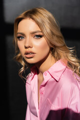 portrait of young woman in pink shirt looking at camera on black background.