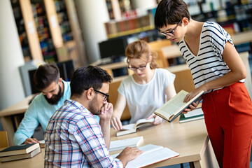 Happy university students studying with books in library. Group of multiracial people in college