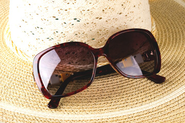 Sunglasses lie on the brim of a wicker hat.