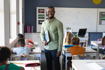 Portrait of smiling african american young male teacher standing by multiracial elementary students - Powered by Adobe