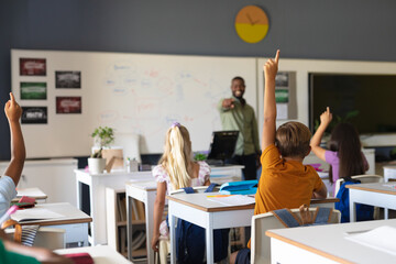 African american young male teacher pointing on multiracial elementary students with hand raised