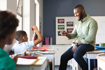 Fototapeta Smiling african american young male teacher gesturing on african american elementary boy at desk obraz