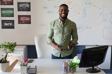 Portrait of african american young male teacher with digital tablet standing against whiteboard
